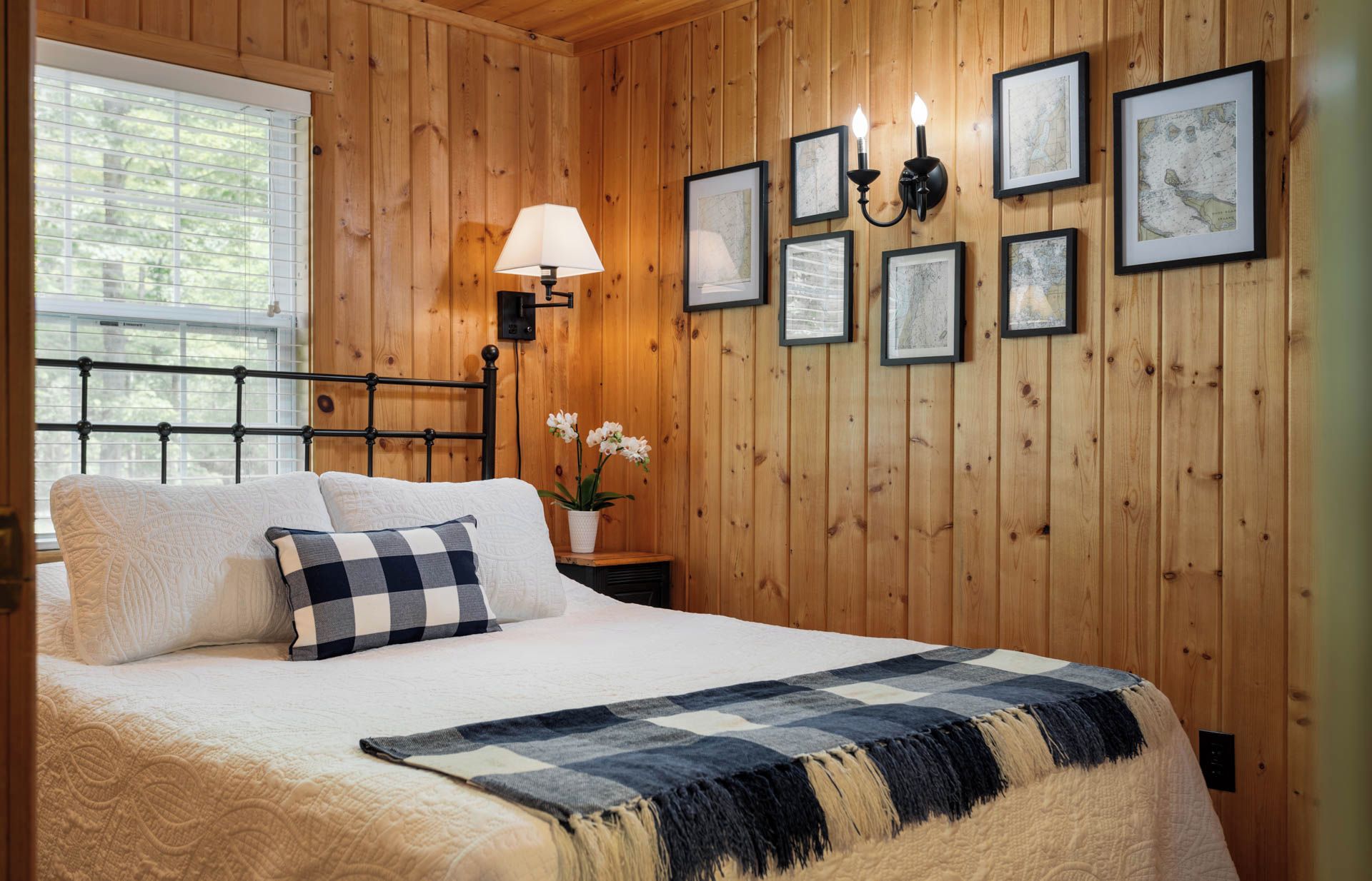 Un dormitorio con paneles de madera, una cama, una mesita de noche, una lámpara y obras de arte enmarcadas en la pared.