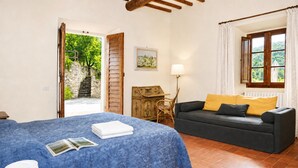Un dormitori amb llit, sofà, làmpada, un quadre a la paret i finestra amb cortines.