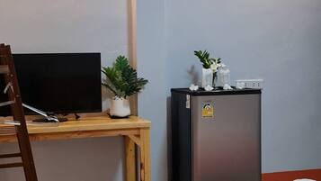 A room with a bed, a desk with a television, a refrigerator, and a potted plant.