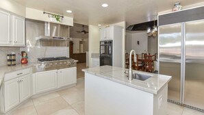 A modern kitchen with white cabinetry, a central island with a sink, a stainless steel refrigerator, and a built-in oven. - WALK TO LA-WHITE SOX SP TRAINING 5MN DRIVE 2 STADIUM 1AC YARD +4Ksq ft HOME (Glendale)