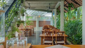 Een restaurant met houten tafels en stoelen, plantenpotten en een trap.
