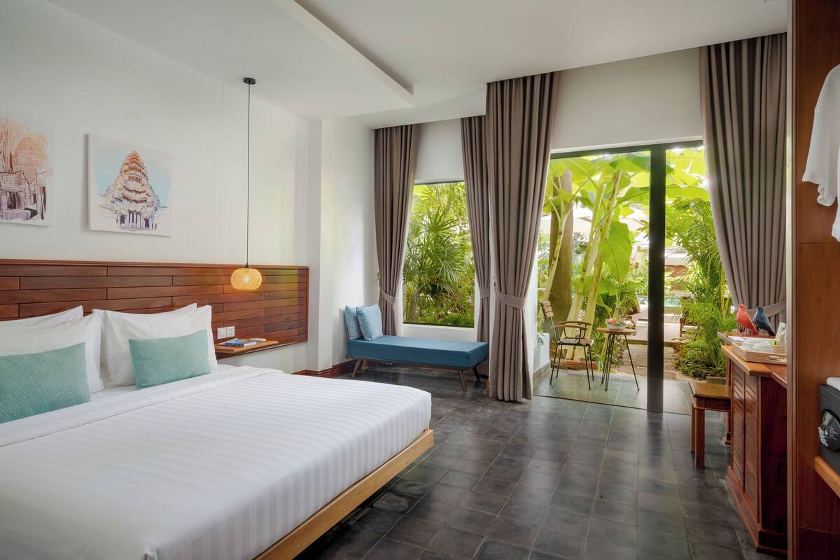 Ein Hotelzimmer mit einem großen Bett, einem Holzkopfteil, einer kleinen Sitzecke und Blick auf Grün.