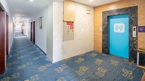 A hotel hallway with patterned carpet, a blue elevator door, and a marble wall. - Hongli Business Hotel (Foshan)
