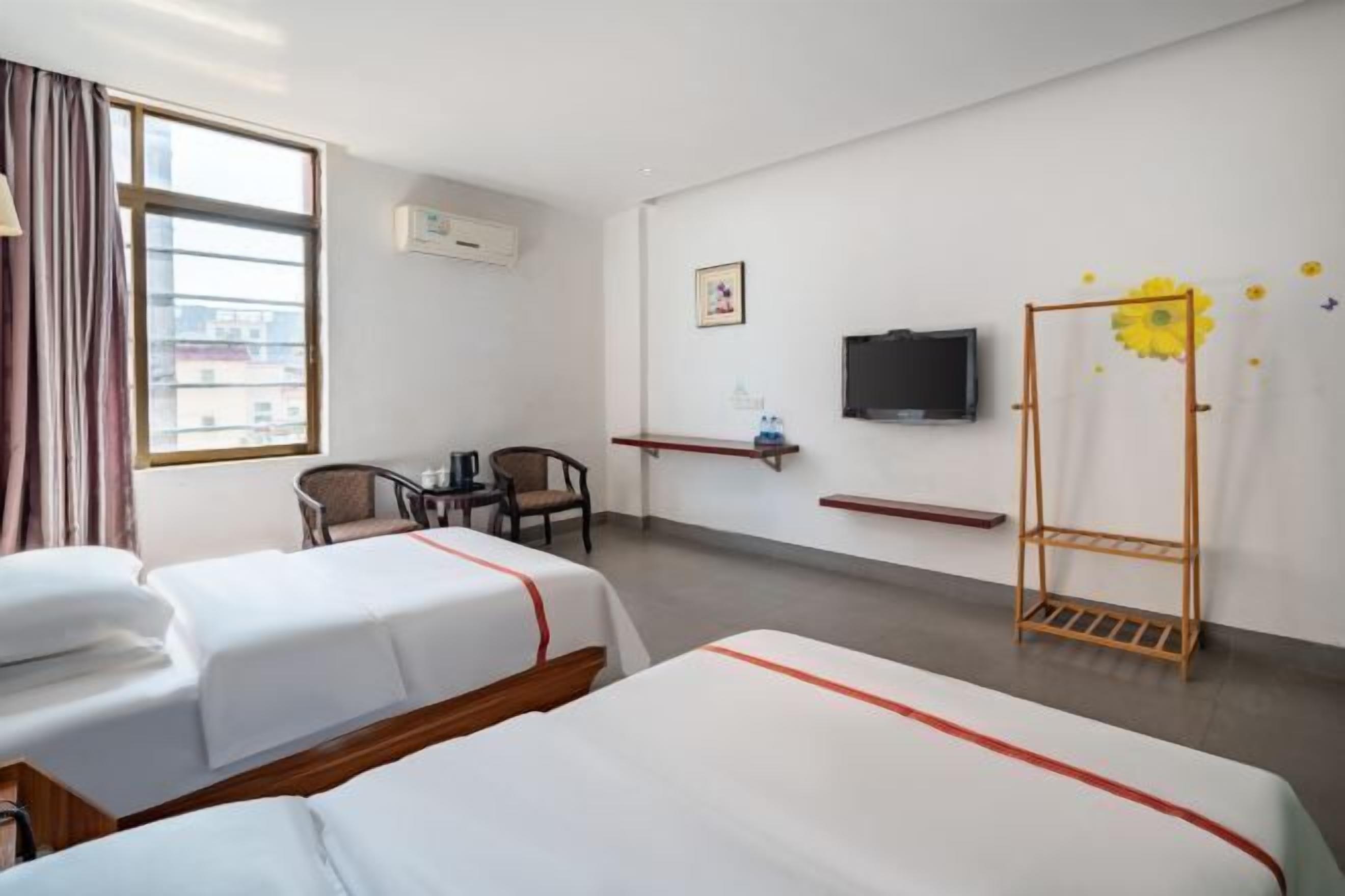 A hotel room with two beds, a desk, a chair, a TV, and a window with curtains.