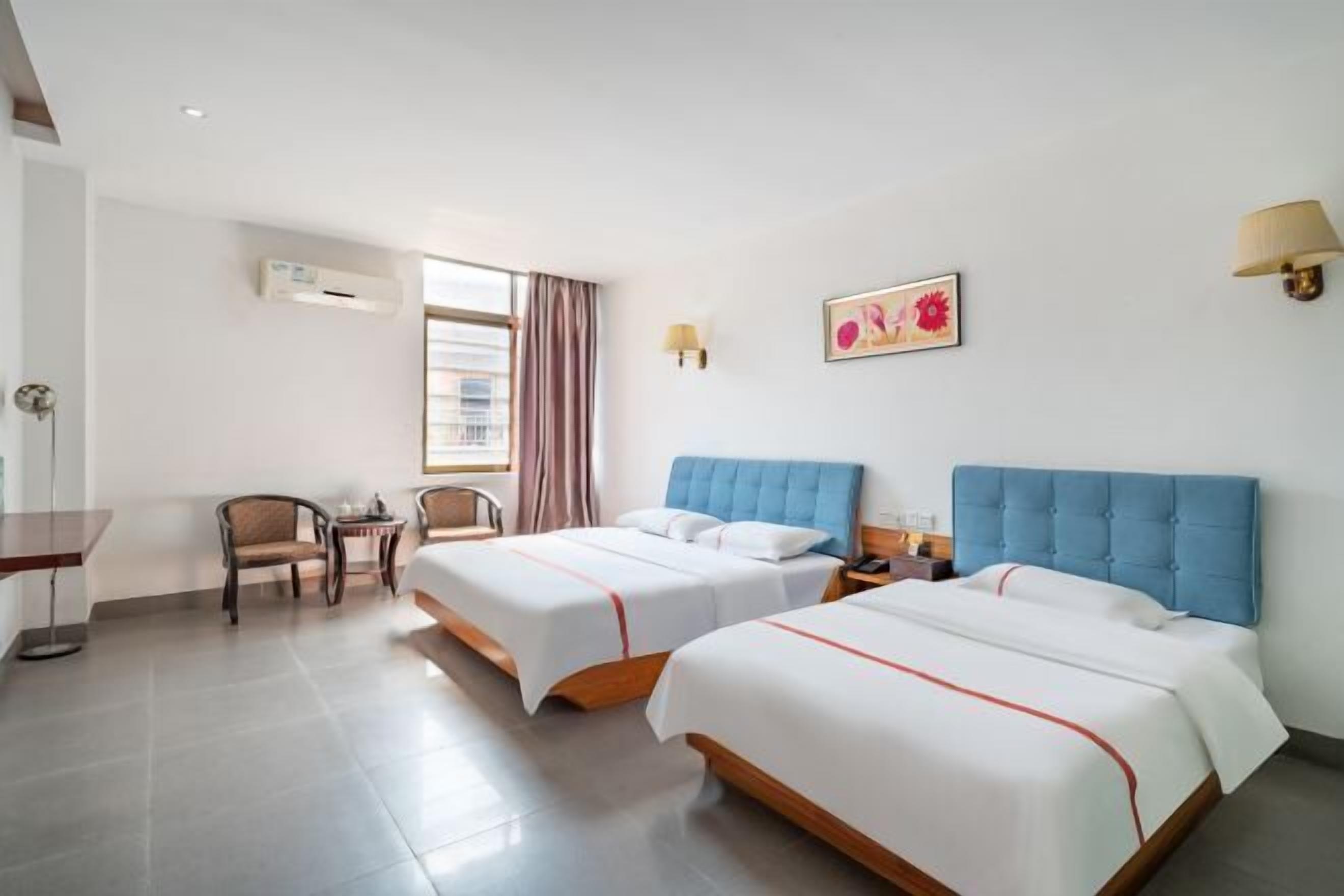 Een hotelkamer met twee bedden, een bureau, een stoel en een raam met gordijnen.