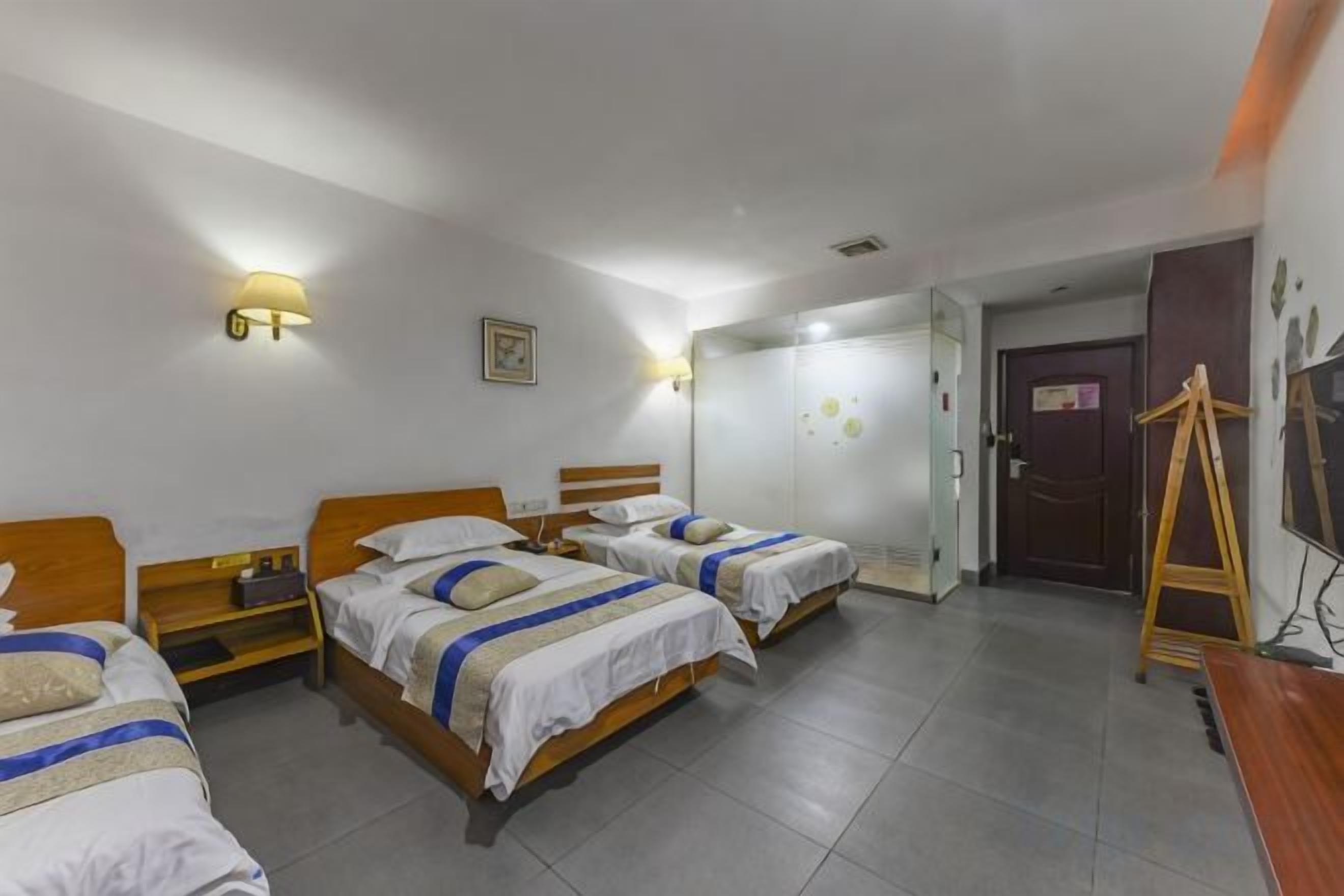 A hotel room with three beds, a wooden dresser, a desk, and a wardrobe.