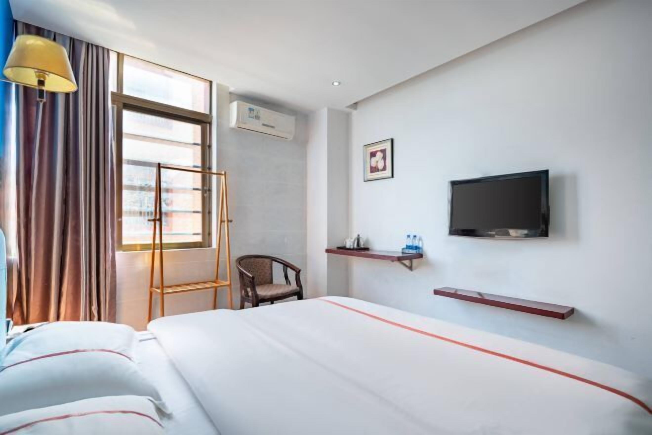 Een hotelkamer met een bed, een stoel, een televisie en een raam met gordijnen.