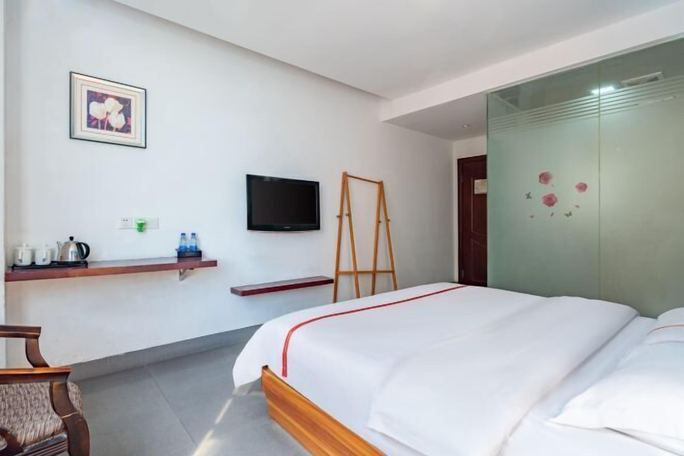 A hotel room with a bed, a television, a shelf with toiletries, and a painting on the wall.