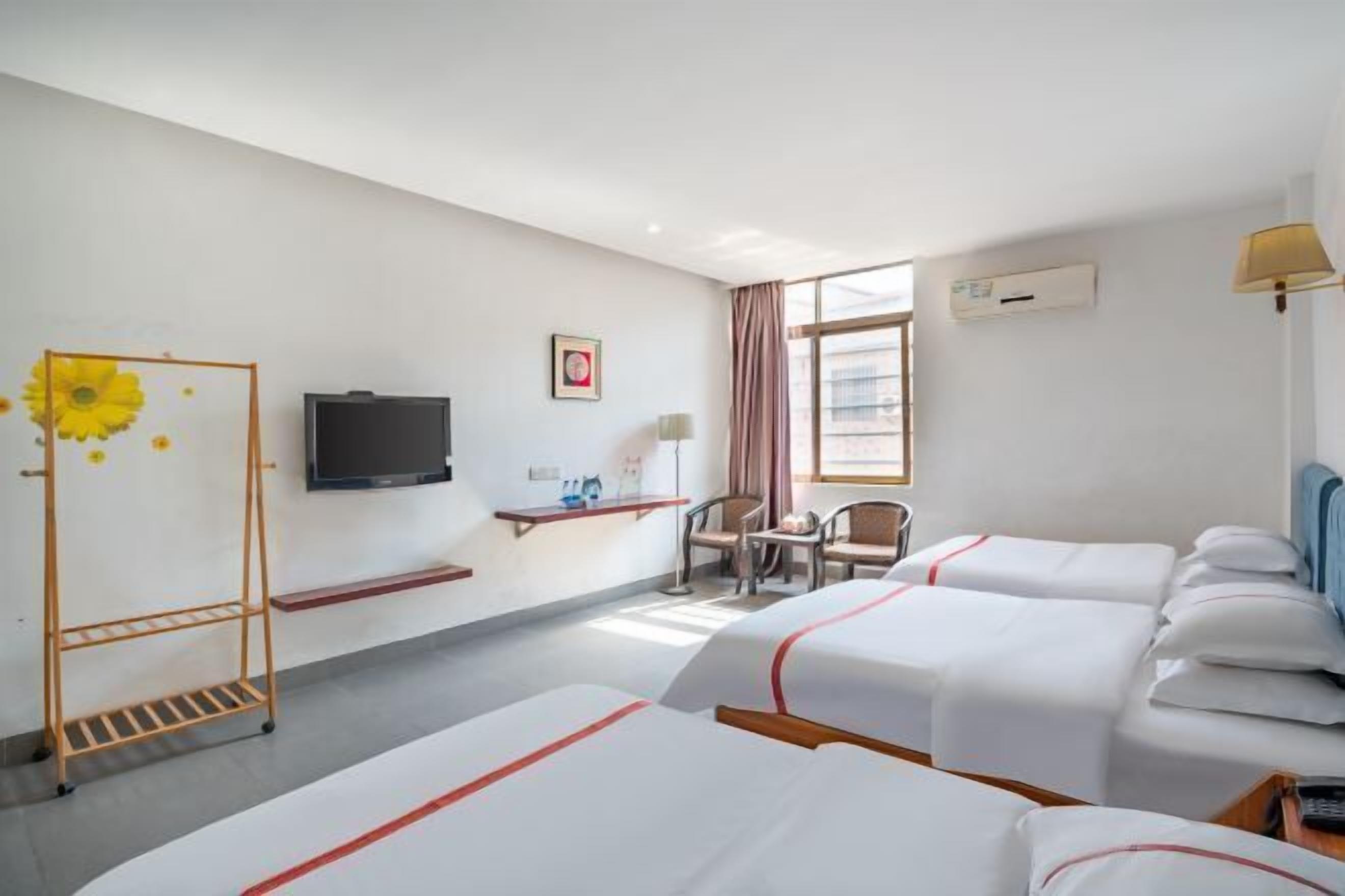 A hotel room with two beds, a TV, a desk with a chair, and a window with curtains.