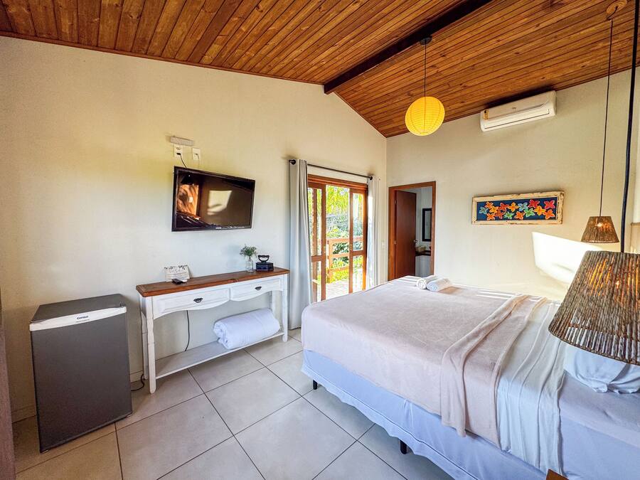 A bedroom with a bed, a desk with a television, a small trash bin, and a door leading to a balcony.