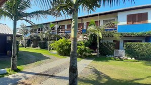 Un hotel con fachada azul y blanca, un espacio cubierto para sentarse al aire libre y un jardín bien cuidado con palmeras y arbustos.