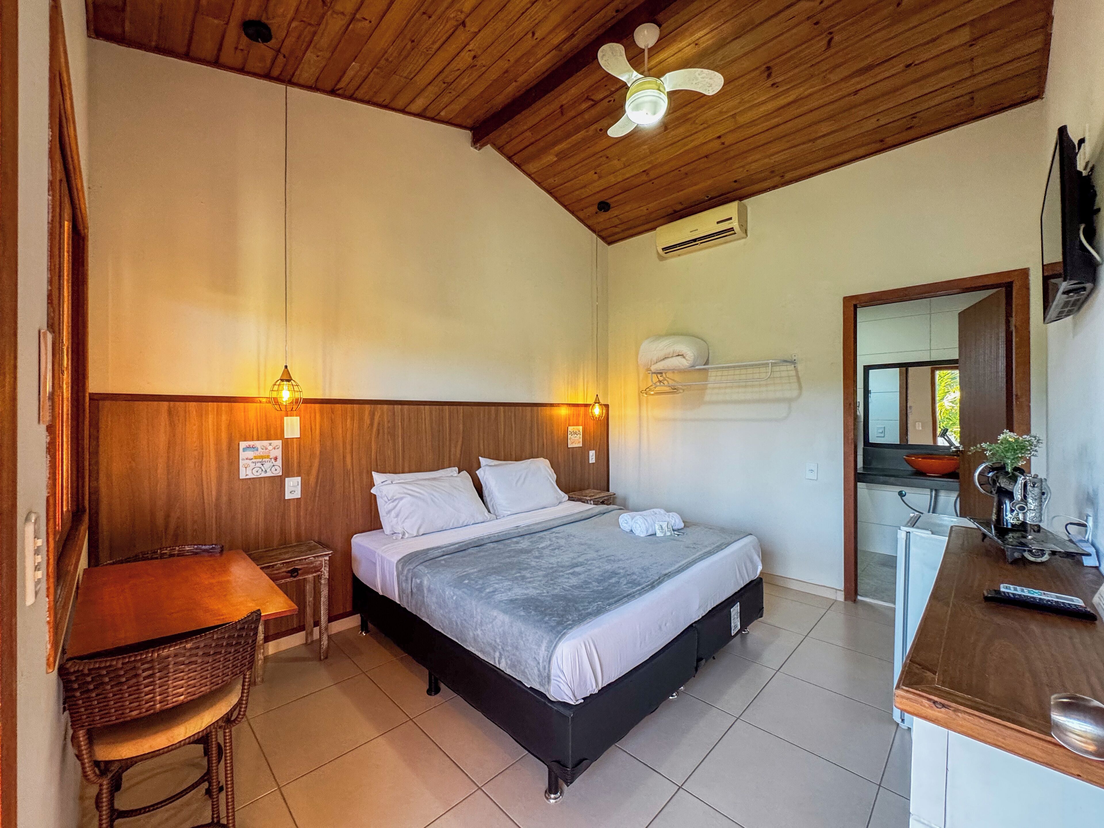 Un dormitorio con cama, mesitas de noche, escritorio, silla, ventilador de techo y espejo.