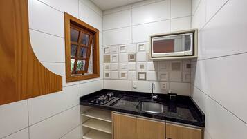 Una cocina compacta con baldosas blancas, encimera negra, estufa integrada, un lavamanos y armarios de madera.