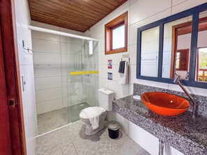 A bathroom with a glass-enclosed shower, a toilet, a sink with an orange basin, and a mirror with a wooden frame.