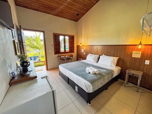 A bedroom with a bed, a small table, chairs, a window, and a view of greenery outside.