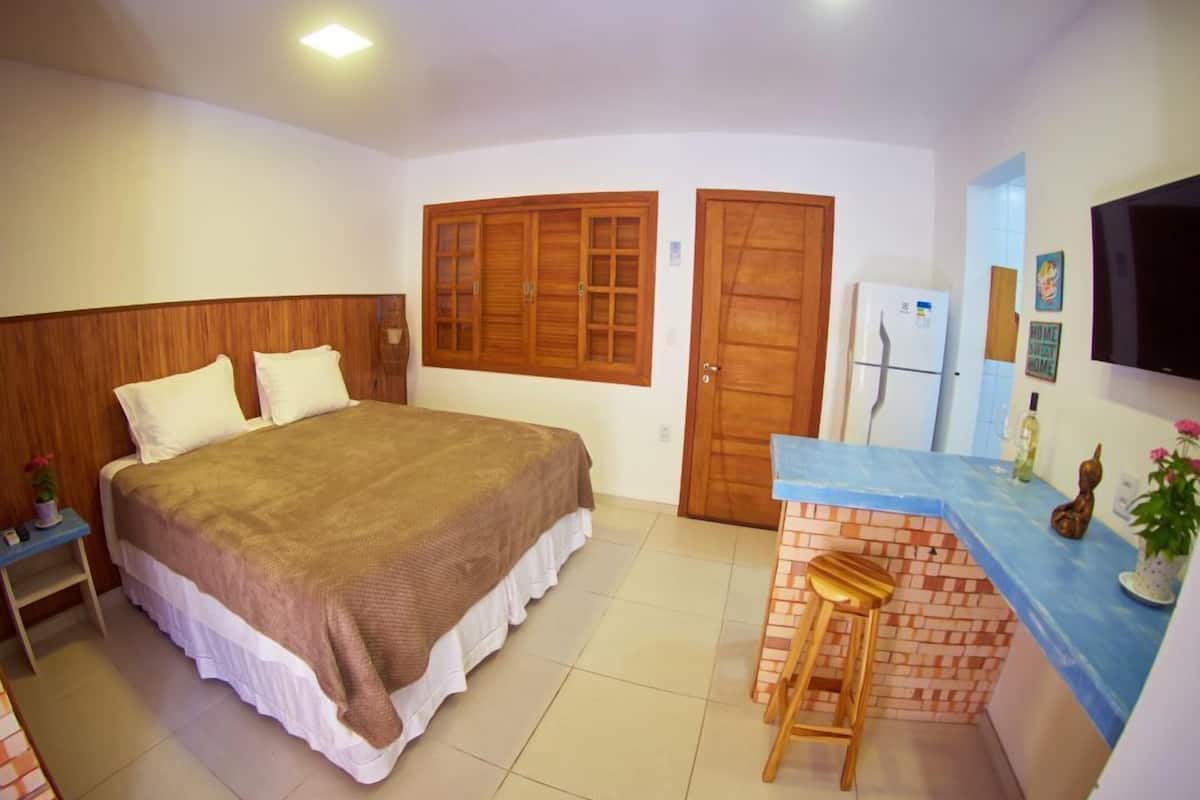 A bedroom with a bed, a small table, a chair, a brick counter, and a TV.