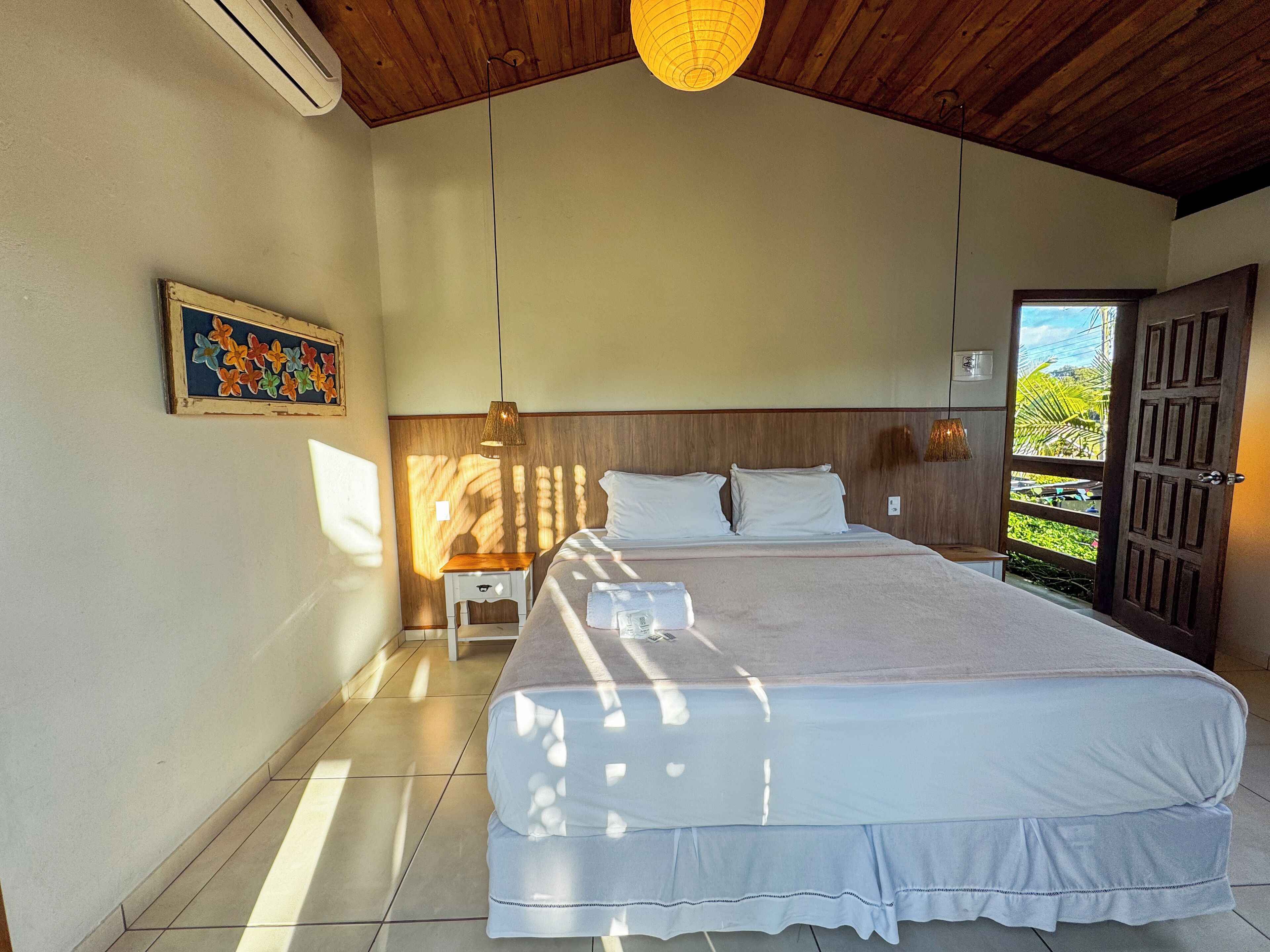 Un dormitorio con una cama grande, una mesita de noche, una lámpara de pared y una puerta que da a un balcón.