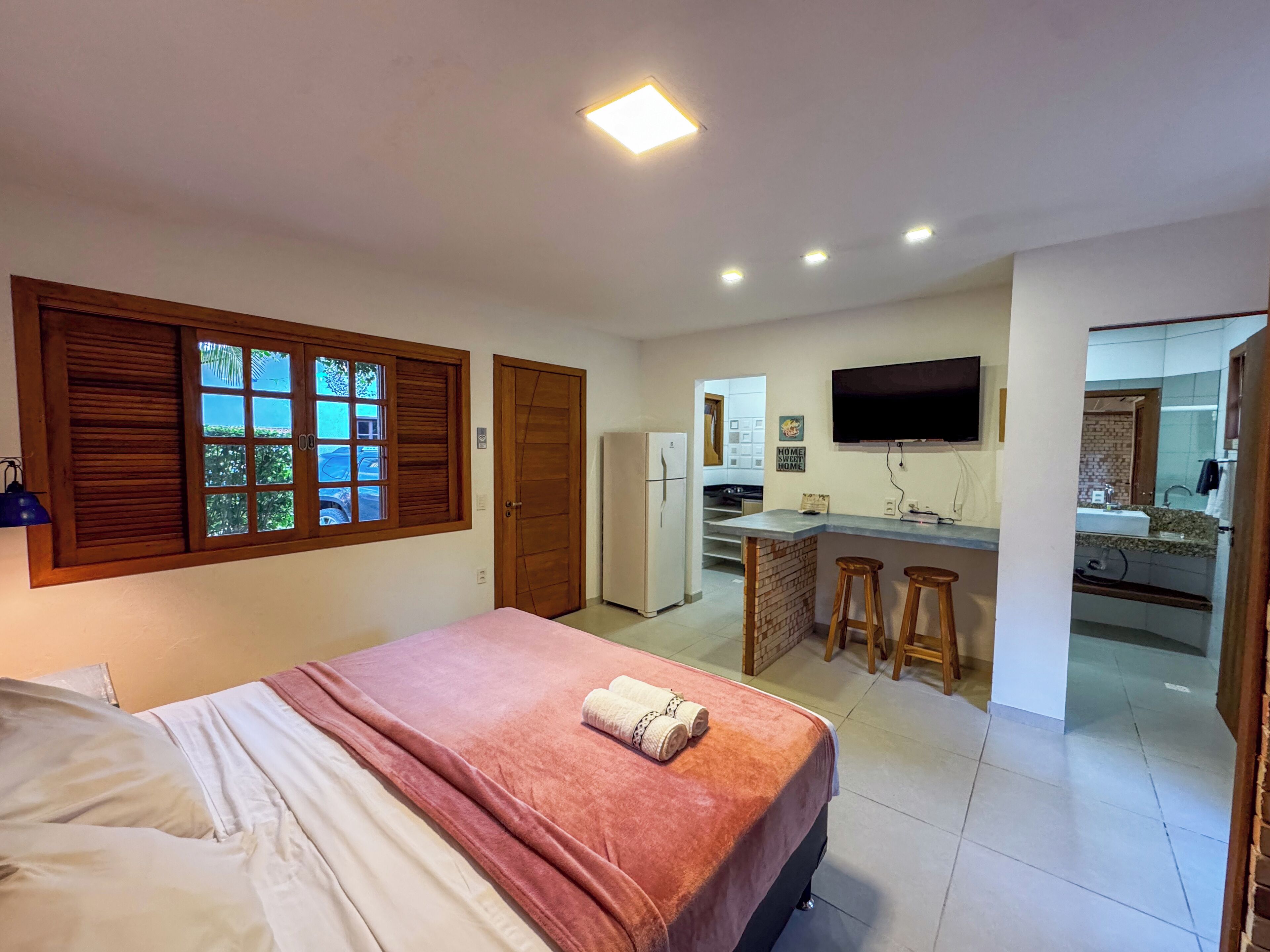 A bedroom with a bed, a kitchen area with a refrigerator, a sink, and a TV.