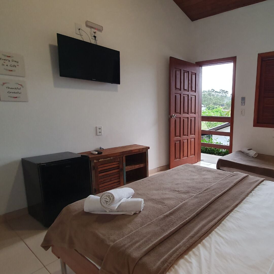 A bedroom with a bed, a wooden dresser, a television mounted on the wall, and a door leading outside.