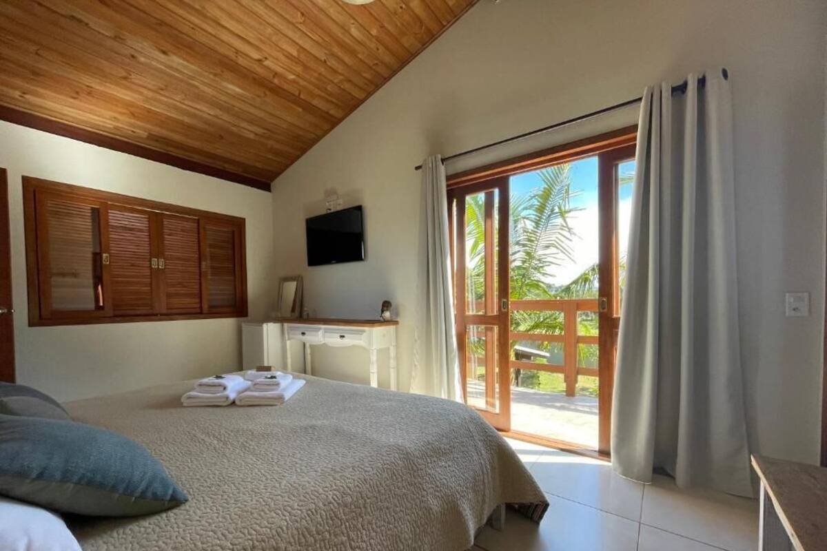 A bedroom with a bed, a TV, a desk, and a sliding glass door leading to a balcony.