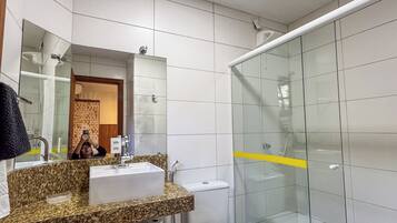 Un baño moderno con lavamanos de granito, espejo, inodoro y cabina de ducha de vidrio.