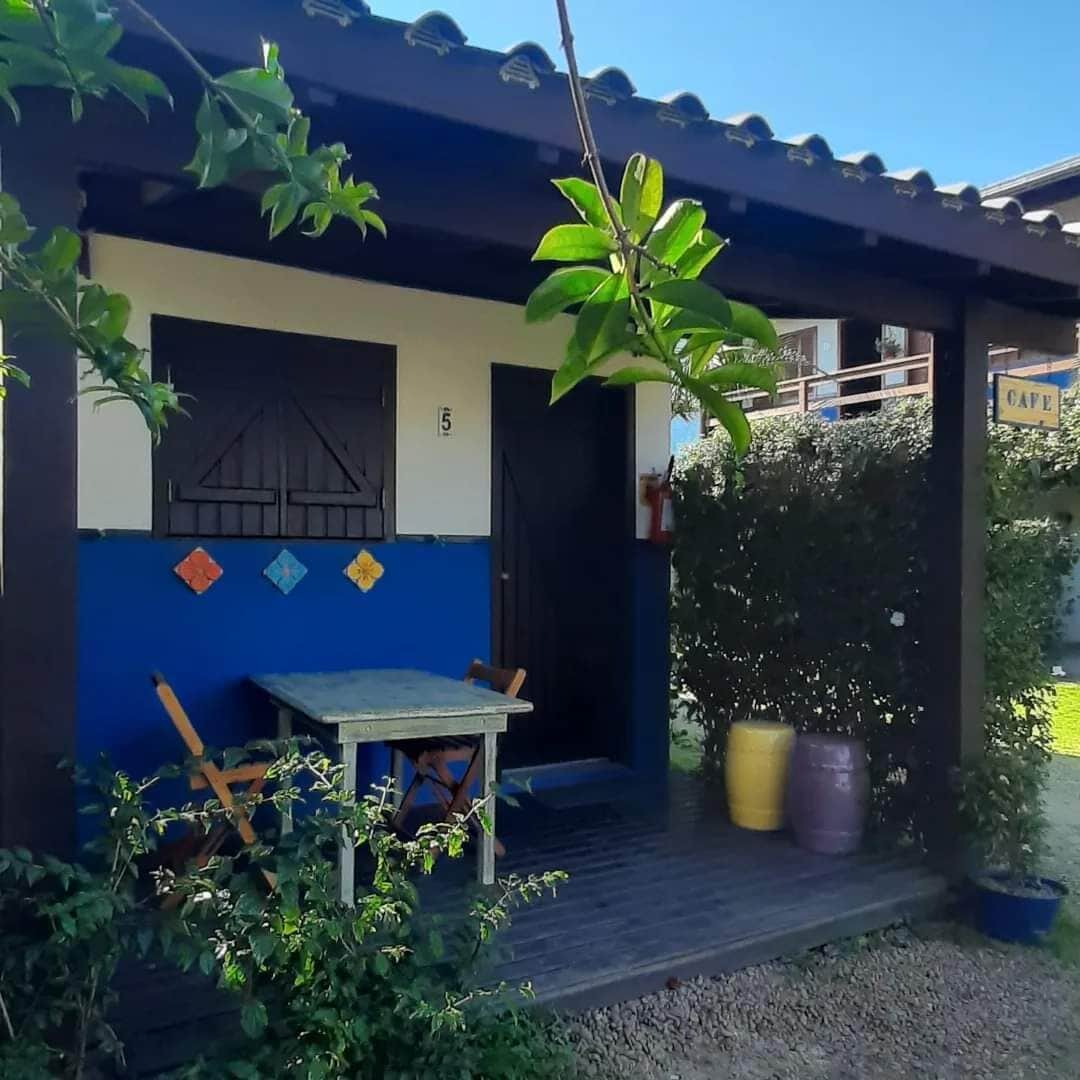 Un edificio con fachada azul y blanca, una puerta de madera, una pequeña mesa y silla afuera, y un letrero que dice "CAFE".