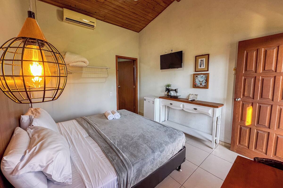 A bedroom with a bed, a wooden ceiling, an air conditioner, a TV, and a wooden door.