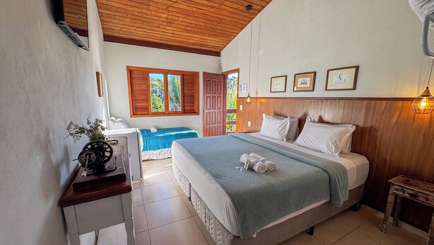 Un dormitorio con una cama grande, un escritorio con una planta y vistas al exterior a través de una ventana con contraventanas.