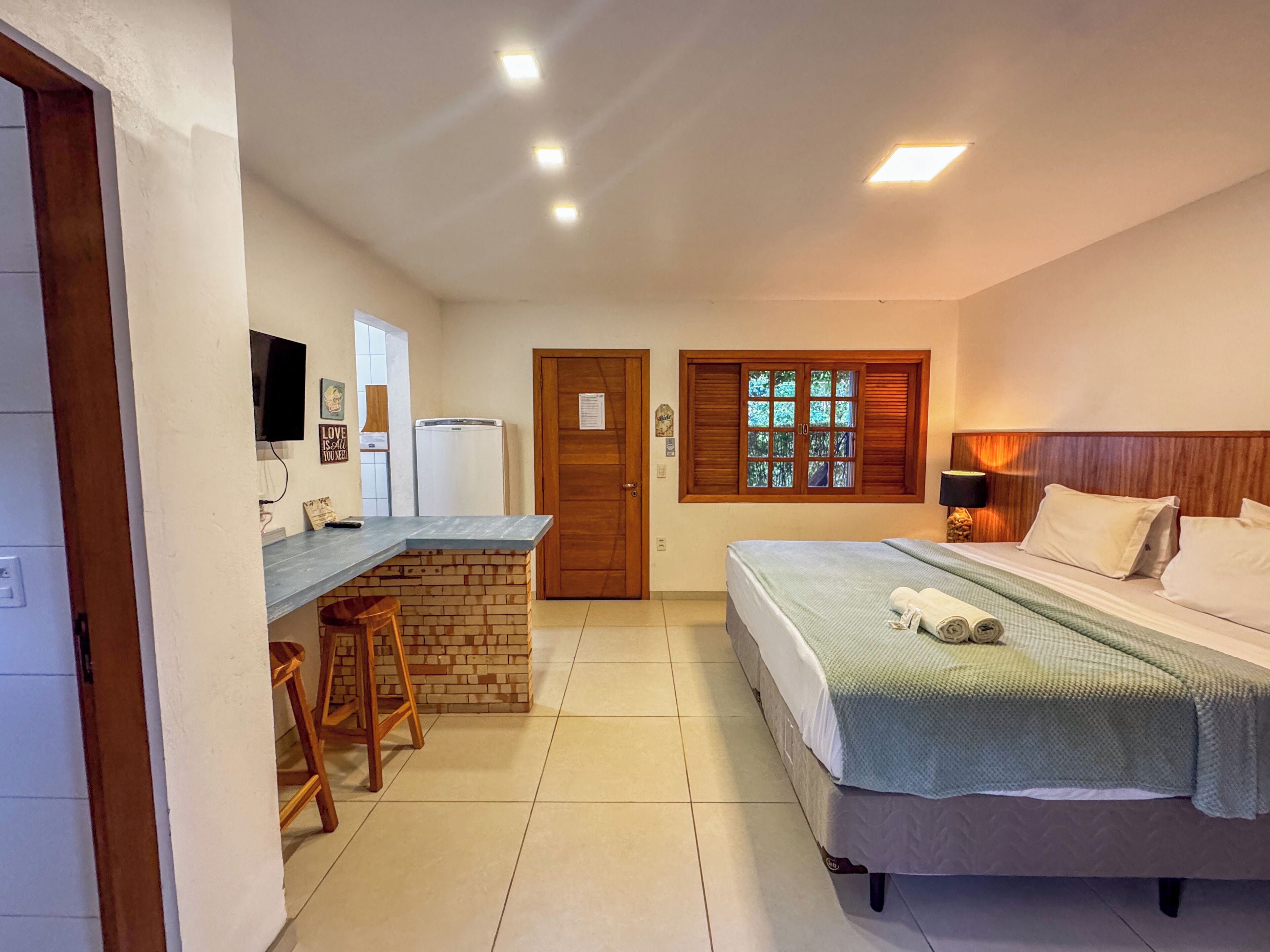 Habitación de hotel compacta con cama, un pequeño escritorio, refrigerador y ventana con contraventanas.
