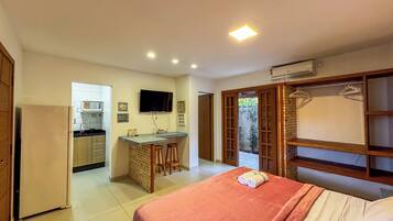 Una habitación de hotel compacta con kitchenette, una cama con una colcha roja y un armario de madera con perchero.
