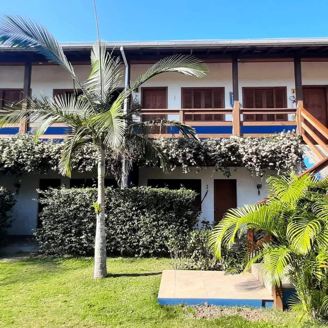 A building with a two-story structure, a balcony with wooden railings, and a covered outdoor area with a palm tree and a small garden.