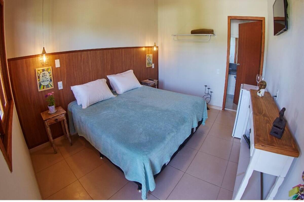 A bedroom with a bed, bedside tables, a desk, a mirror, and a door.