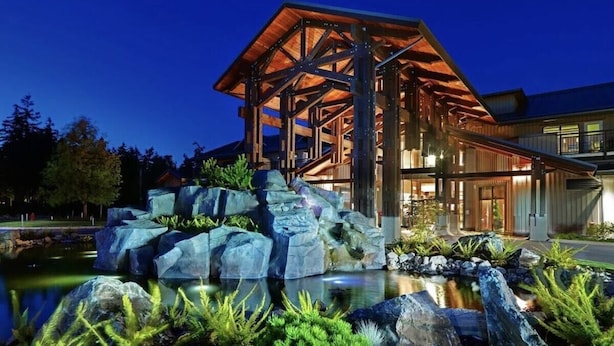 Un bâtiment moderne à la structure en bois, avec un bassin agrémenté de rochers et de plantes.