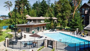 Un espace piscine doté d’une terrasse entourée d’une clôture, de chaises longues et d’un bâtiment avec une grande fenêtre donnant sur la piscine.