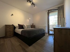 Ein Schlafzimmer mit Bett, Kommode, Schreibtisch und einem Fenster mit Vorhängen.