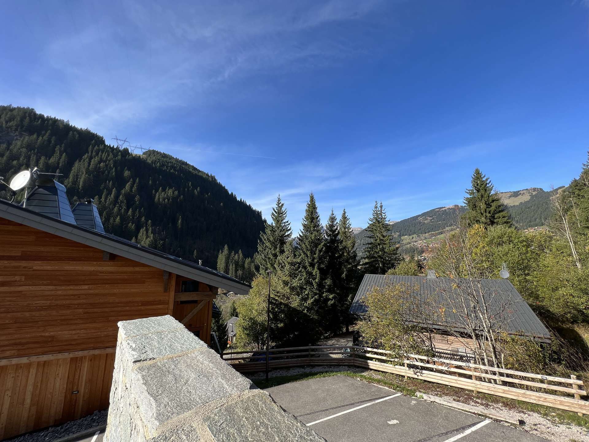 A wooden cabin with a stone wall, a parking area, and a mountainous backdrop.