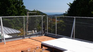 Una terraza de madera con sillones blancos y una mesa, rodeada por una valla de metal.
