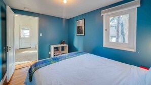 Une chambre avec un lit, une petite table console blanche, un tableau au mur et une fenêtre donnant sur des arbres.