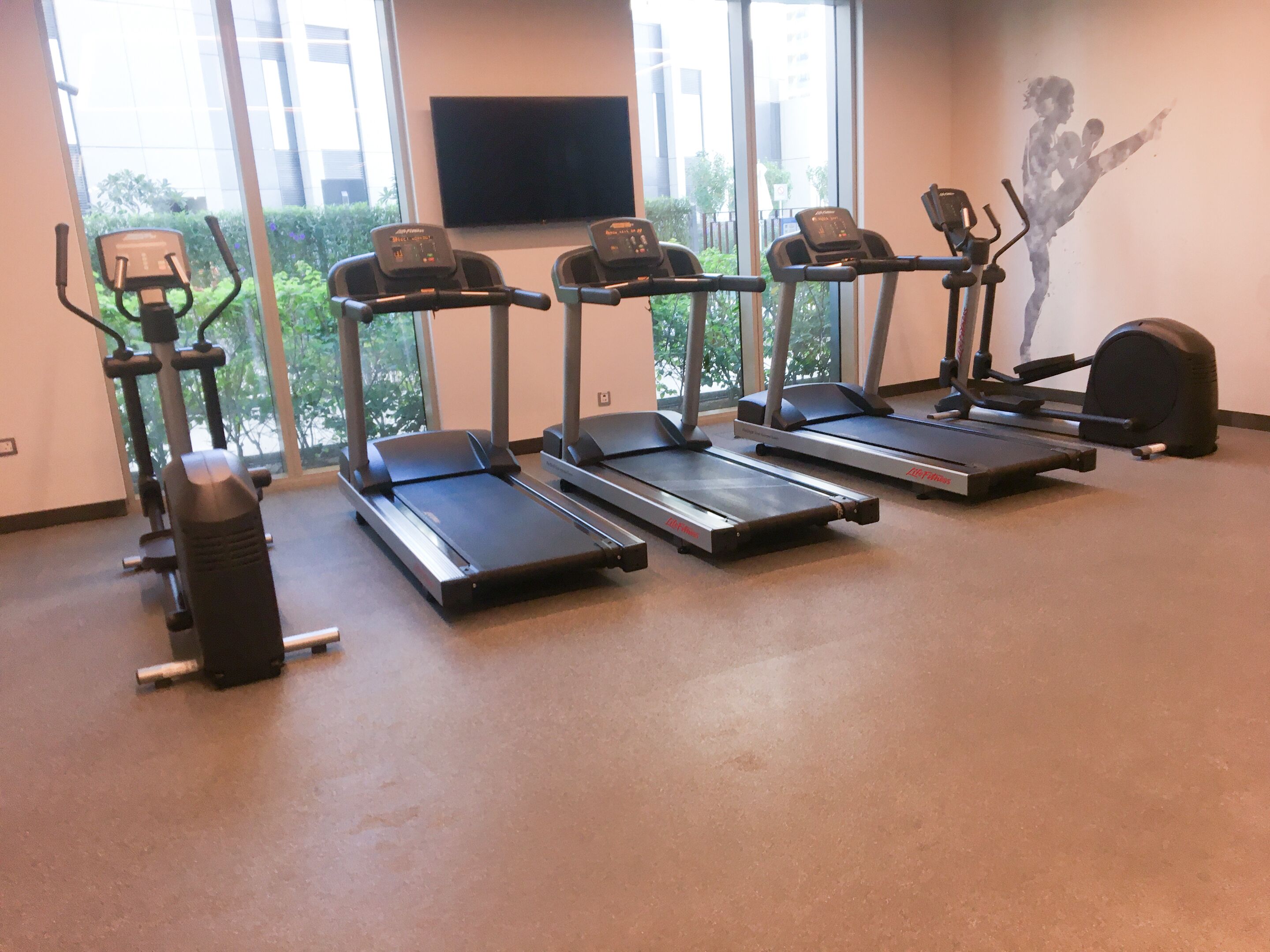 Ein Fitnessraum mit Laufbändern, einem Ergometer und einem wandmontierten Fernseher.