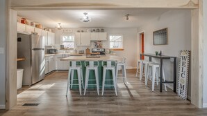 A modern kitchen with white cabinets, a central island with bar stools, and a 'WELCOME' sign. - Charming open 4bd and screen-in porch! Sleeps 10! (Saint Charles)