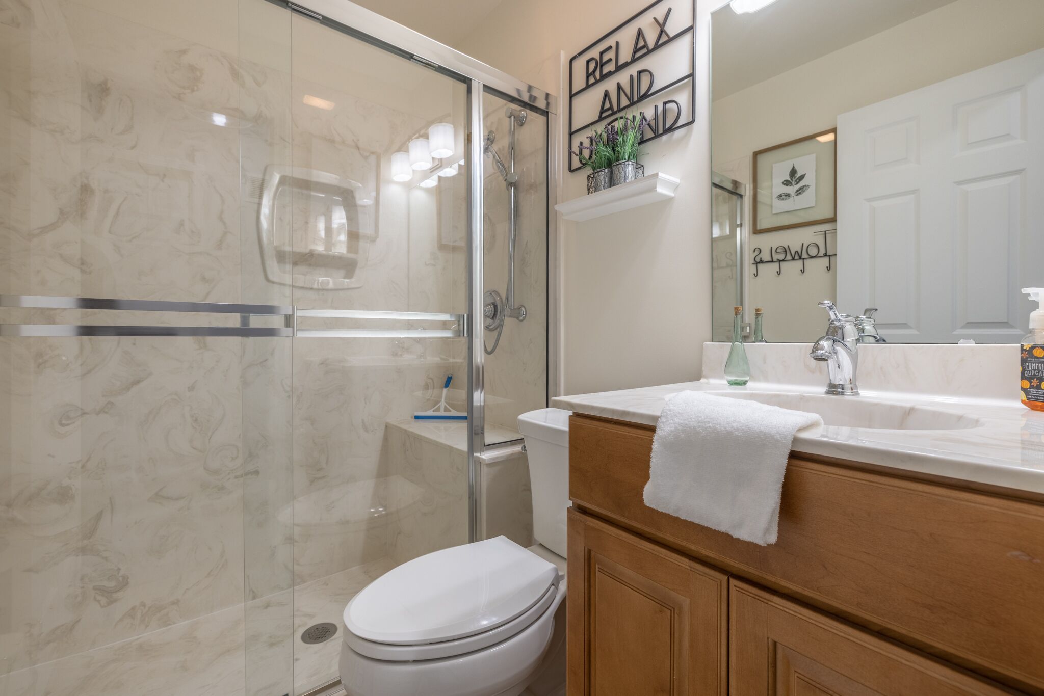 Une salle de bain avec une douche à parois de verre, des toilettes blanches, un lavabo avec une serviette blanche, et un miroir sur lequel est inscrit : « DÉTENTE ET DÉCOUVERTE ».