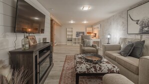 A modern living room with a flat-screen TV, a sofa, a coffee table, and a fireplace. - Charming open 4bd and screen-in porch! Sleeps 10! (Saint Charles)