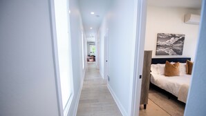 Un pasillo que conduce a un dormitorio con una cama, una mesita de noche y una obra de arte colgada en la pared.