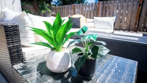 Un sofá de mimbre con cojines blancos y una mesa de vidrio con dos plantas en macetas.