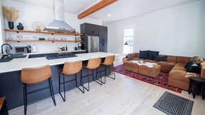 Una cocina moderna con una isla central, taburetes de bar y una zona de comedor con sofá y mesa de centro.