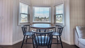 A bay window with three chairs and a table, wooden walls, and a view of trees and buildings. - Canyon View Ski House | Sleeps 14 + Hot Tub (Cottonwood Heights)