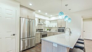 A modern kitchen with stainless steel appliances, a central island, and pendant lighting. - Canyon View Ski House | Sleeps 14 + Hot Tub (Cottonwood Heights)