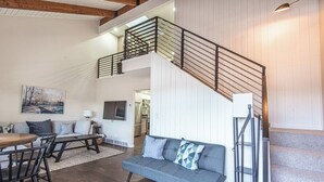A spacious living area with a grey sofa, a dining table with chairs, a staircase with a railing, and a painting on the wall. - Canyon View Ski House | Sleeps 14 + Hot Tub (Cottonwood Heights)