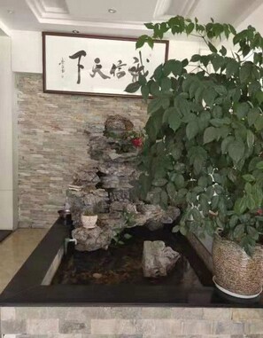 Une pièce avec un mur en pierre, une œuvre calligraphique encadrée et une grande plante en pot.