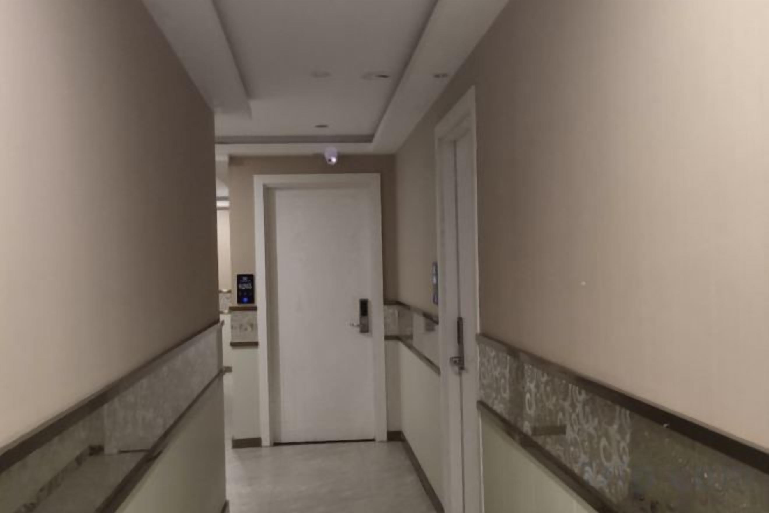A corridor with a door at the end, a handrail on the left, and a wall-mounted light fixture.